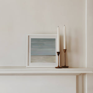 After The Rain limited edition paper print in white frame on mantelpiece with brass candles – abstract seascape wall art DT Art Studio.